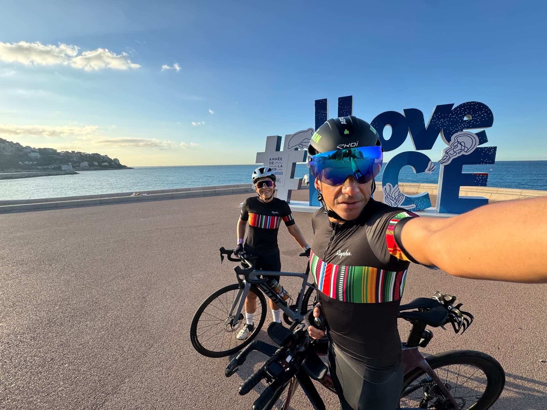 Rodrigo y Rox en bicicleta frente al letrero I Love Nice al amanecer.